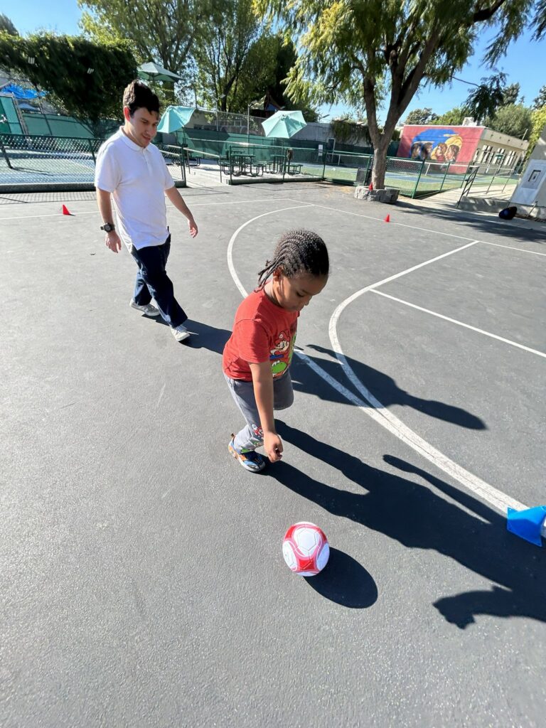 Young boy playing soccer outside on school playground.