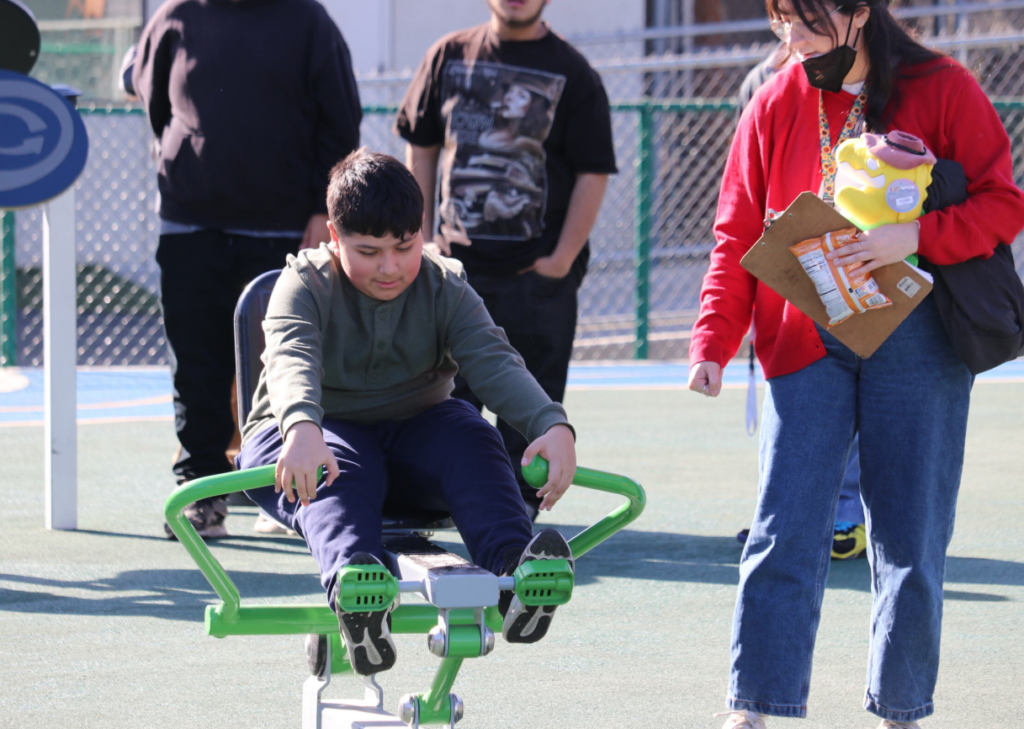 Consistent Play - boy using exercise equipment with teacher's aide at school playground